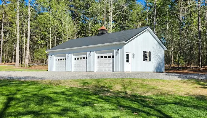 light blue and white three car pole barn garage with an entry door, windows, and a cupola